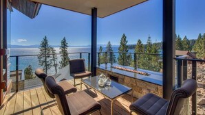 Un balcon doté d’une balustrade en verre, d’une cheminée en pierre et offrant une vue sur l’océan et les arbres.
