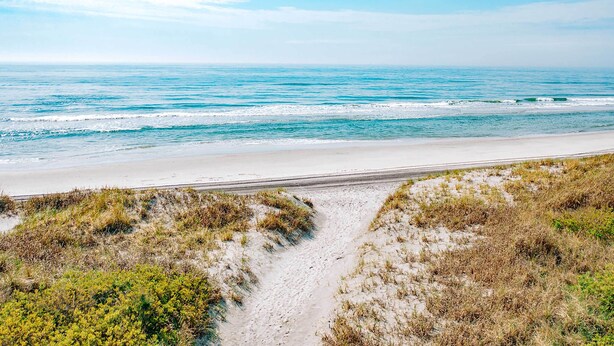 A beach with a sandy path leading to the water, surrounded by grassy dunes.