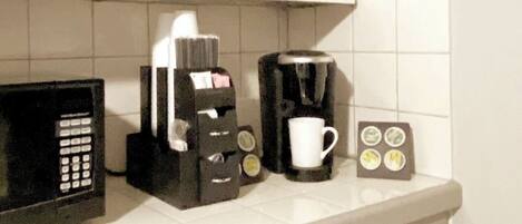 A kitchen counter with a microwave, coffee maker, and a coffee pod holder.