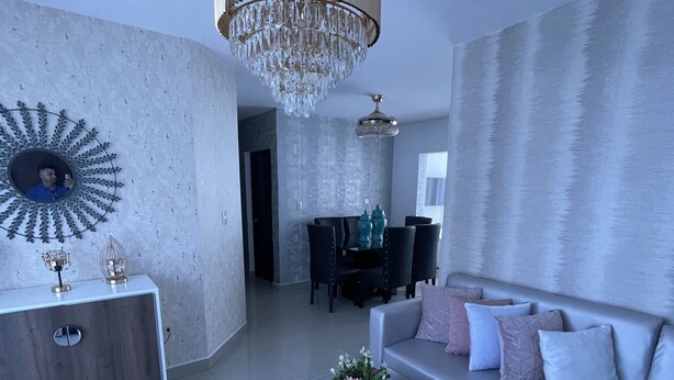Uma sala de estar moderna com um sofá cinzento, uma mesa de centro de vidro e um candelabro.