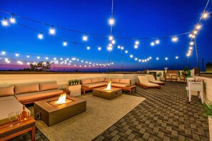 A rooftop terrace with outdoor seating, fire pits, and string lights against a twilight sky. - Bachelorette Bash! Sleeps 20! 2 Private rooftops! (Nashville)
