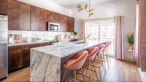 A modern kitchen with dark wooden cabinets, a marble island, and pink bar stools.
