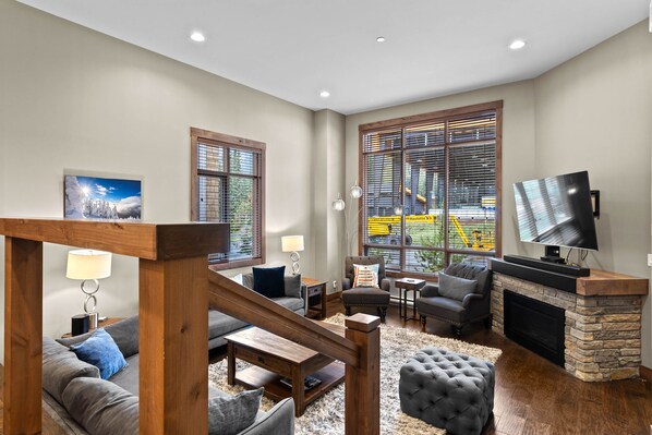 A spacious living room with a fireplace, large windows, and a television. - Villagewalk #11 | 3 Peaks Rentals (Sun Peaks)