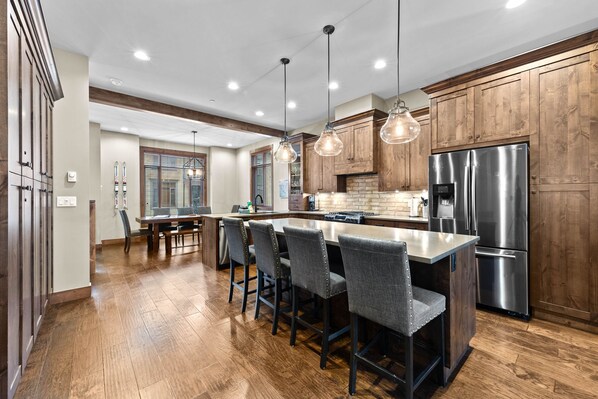 A modern kitchen with wooden cabinets, a stainless steel refrigerator, and pendant lighting.