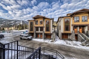 A modern multi-story building with a stone facade, large windows, and a staircase leading to the entrance. - Villagewalk #11 | 3 Peaks Rentals (Sun Peaks)