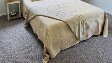 Ein Schlafzimmer mit Bett, Nachttisch, Lampe, Deckenventilator, Fenster mit Vorhängen und einem Wandbild.