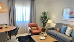 Un salon moderne avec une table à manger ronde, un canapé agrémenté de plusieurs coussins, une table basse et une plante en pot.