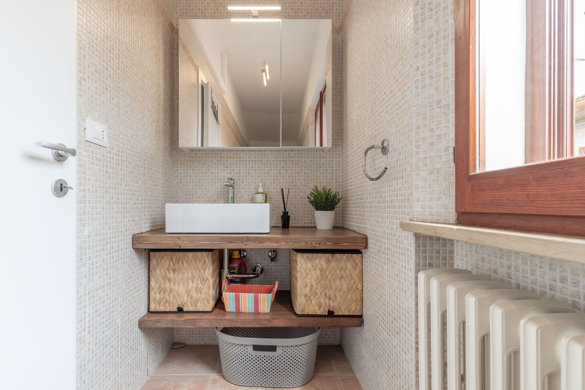A bathroom with a white sink, wooden vanity, a mirror, and a radiator.