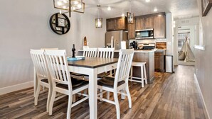 A modern kitchen with wooden cabinets, a central island, and a dining area with white chairs and a wooden table. - Moose Meadows Escape in McCall - dog friendly & 1 bed/1 bath on each of 3 floors (McCall)