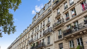 A multi-story building with balconies, large windows, and a blue awning. - Studio Listelli - Welkeys (Paris)