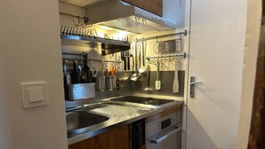 A compact kitchen with a stainless steel sink, a built-in oven, and a hanging rack for utensils. - Studio Listelli - Welkeys (Paris)