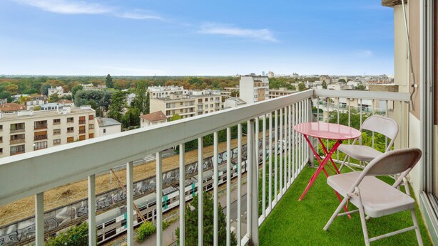 A balcony with a view of a cityscape, a small table, and two chairs. - Appartement Libération - Welkeys (Vincennes)