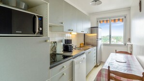 A modern kitchen with a microwave, toaster, and dishwasher. There's a dining table with chairs and a view of the outdoors through a window. - Appartement Libération - Welkeys (Vincennes)