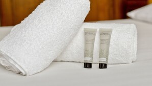 A neatly folded white towel and two Zennao Ginseng shower gel tubes on a bed. - Appartement Libération - Welkeys (Vincennes)