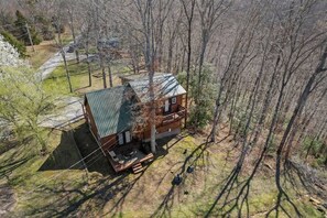 Een chalet met een groen dak, omringd door bomen, en een klein terras.