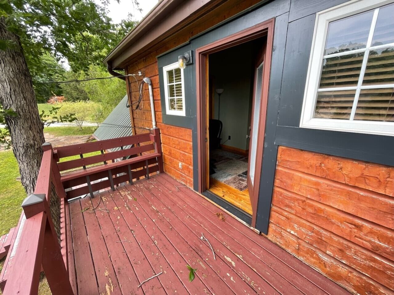 Terraza de madera con un banco, una puerta que da al interior y una ventana con persianas.