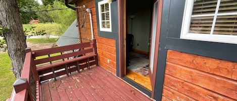 Terraza de madera con un banco, una puerta que da al interior y una ventana con persianas.