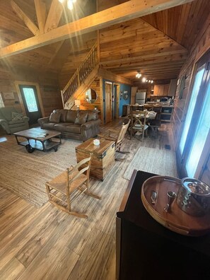 Amplia sala de estar con piso de madera, un sofá, una mesa de centro y una mesa de comedor con sillas. Una escalera conduce a un nivel superior.