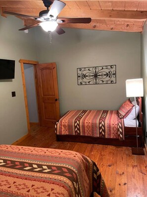 Een slaapkamer met twee bedden, een plafondventilator, een tv aan de muur en een decoratief metalen object.