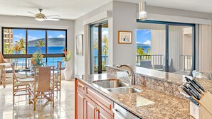 A modern kitchen with a granite countertop, stainless steel sink, and a dining area with wicker chairs.