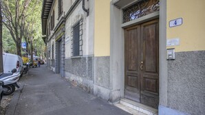 A narrow street with parked scooters and a white van, a building with a large wooden door, and a blue parking sign. - Myosotis - Sweet Dreams in Florence (Firenze)