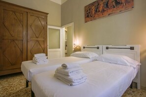 A hotel room with two beds, a large wooden wardrobe, and a painting on the wall.