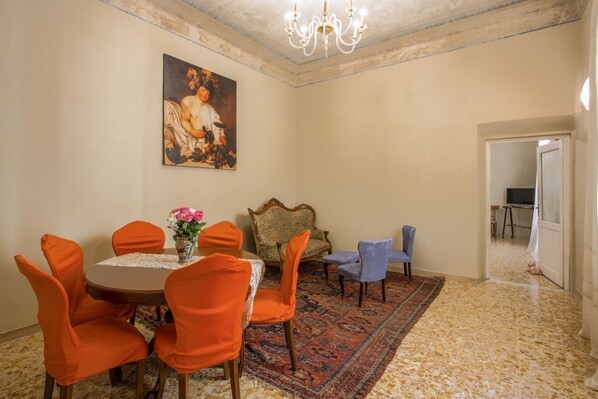 A dining area with a round table, orange chairs, a floral centerpiece, and a large painting on the wall.