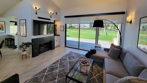 A modern living room with a fireplace, a sofa, a coffee table, and a large sliding glass door leading to a green outdoor area.