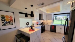 A modern kitchen with a central island, pendant lighting, and a view of a green landscape.