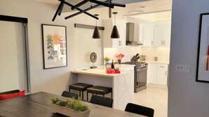 A modern kitchen with white cabinets, a central island, pendant lighting, and a dining area with a wooden table and chairs.