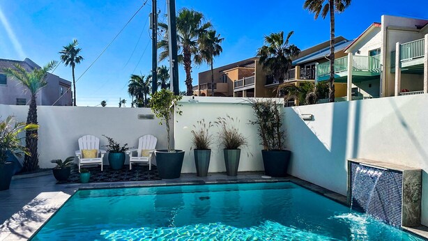 Una piscina con agua cristalina, rodeada de plantas en macetas y una silla blanca.