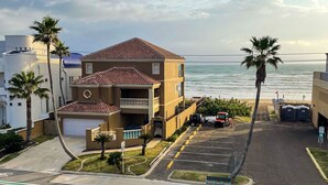 Un edificio de varios pisos con estacionamiento, vista a la playa y palmeras.