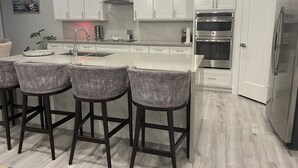 Una cocina moderna con armarios blancos, electrodomésticos de acero inoxidable y una isla central con taburetes de bar.