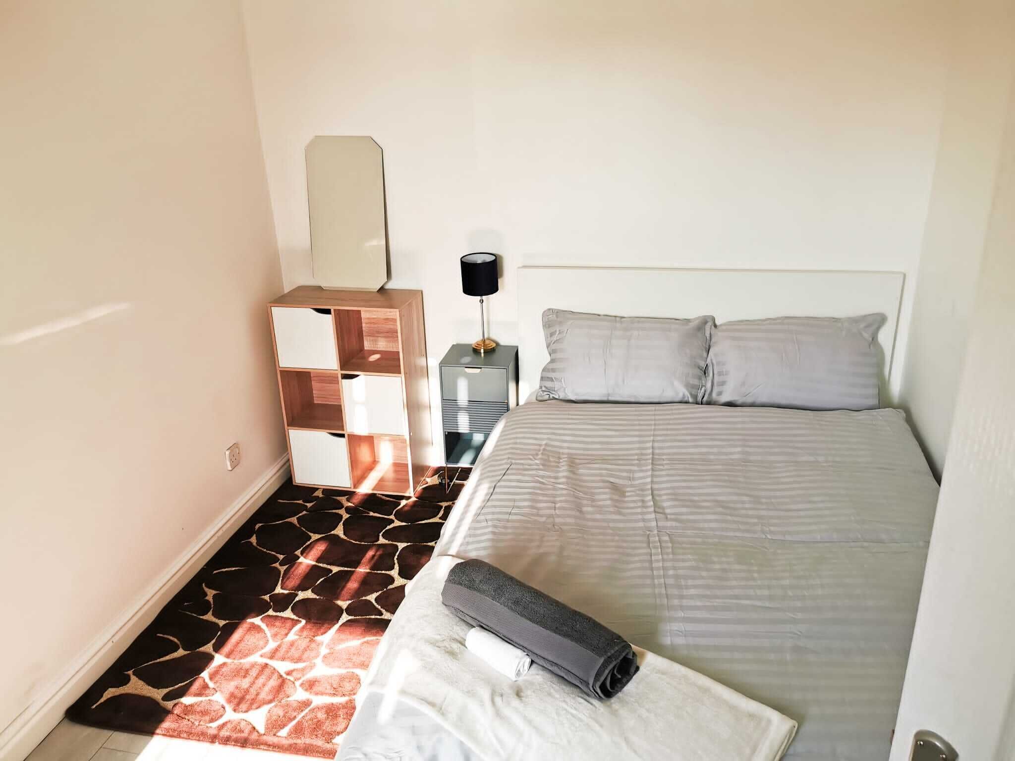 Un dormitorio con cama, mesita de noche, cómoda y alfombra estampada con jirafas.