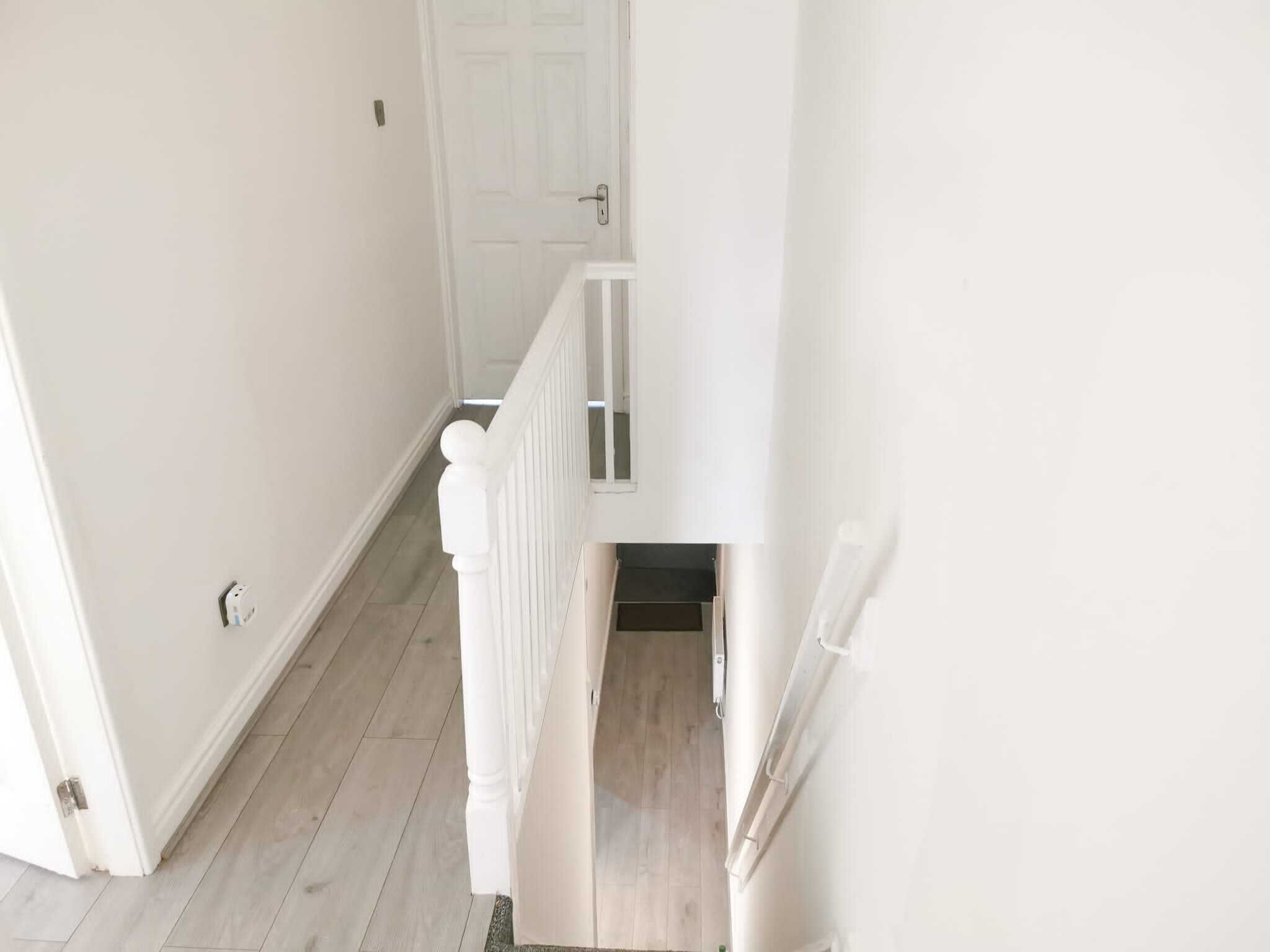 A narrow hallway with a wooden floor and white walls, leading to a door at the end.