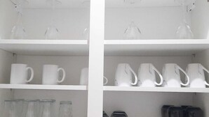 En hvid hylde med forskelligt glas, heriblandt klare og hvide krus samt glasflasker.