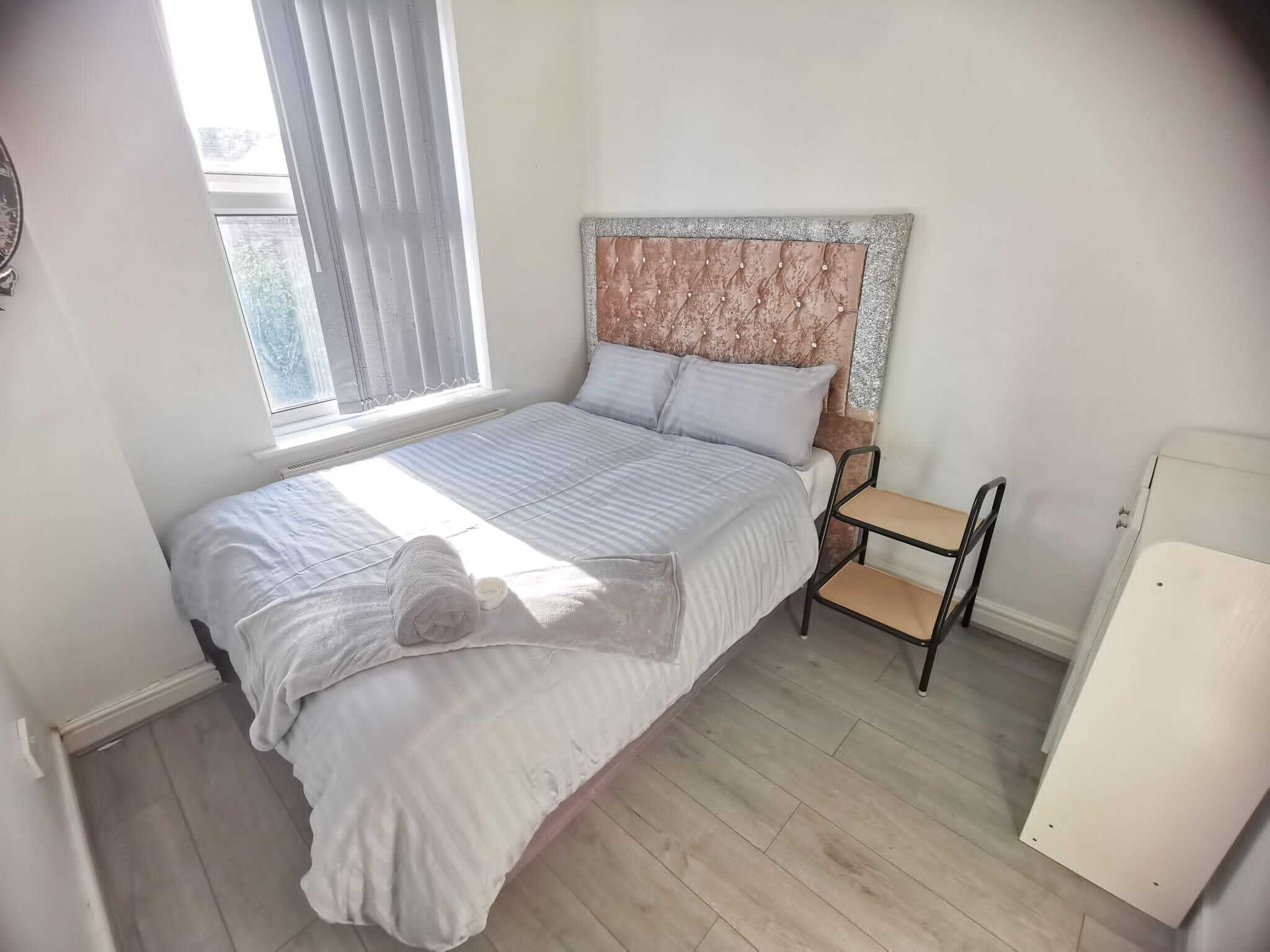 Un dormitorio con cama, mesita de noche, silla y una pequeña mesa.