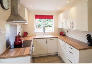 A modern kitchen with white cabinets, a stainless steel range hood, a red kettle, and a window with a red valance.