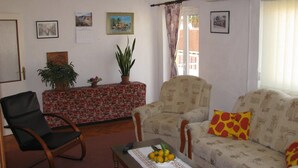 A living room with a sofa, a chair, a table with fruit, a potted plant, and a calendar on the wall. - waterfront apartment family friendly, ground level (Dubrovnik)
