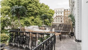 A balcony with wicker furniture, a decorative metal railing, and a large tree in the background.
