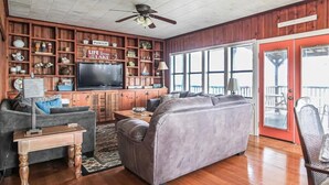 A living room with a large gray sectional sofa, a wooden entertainment center, and a television. - The Lily Pad (Lake Providence)