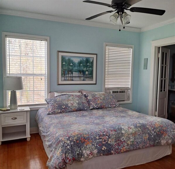 A bedroom with a bed, a ceiling fan, and two windows with blinds.