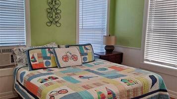 Une chambre avec un grand lit, des murs verts et trois fenêtres équipées de stores.