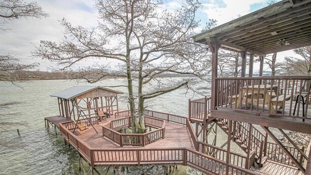 A wooden dock structure with a central tree surrounded by a circular railing, extending over water. - The Lily Pad (Lake Providence)