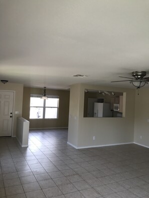 Relax in this airy living space with a high ceiling and ceiling fan, featuring a large window and door to a kitchen area.