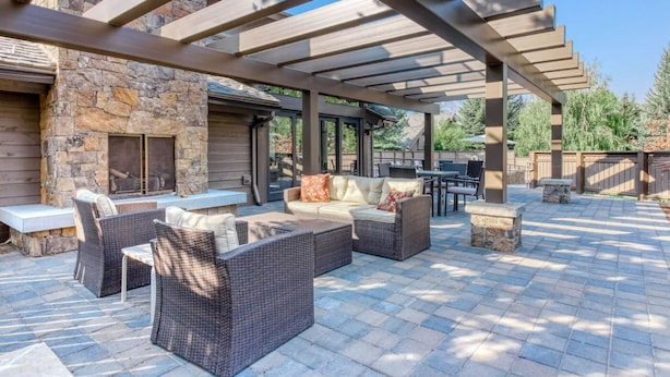 Un patio exterior con suelo de piedra, mobiliario de mimbre y chimenea de piedra.