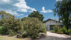 A modern house with a gravel driveway, surrounded by dense vegetation and a clear blue sky. - Riverport Retreat - Pet Friendly, close to the river, free Wifi + linen included (Goolwa South)