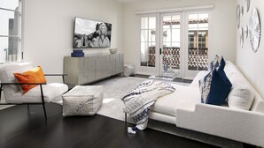 A modern living room with a sofa, armchair, and ottoman. There is a television mounted on the wall and a ceiling fan. - Luxury Top Floor Condo in Heart of Downtown Santa Barbara  (Santa Barbara)
