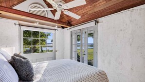 A bedroom with a bed, a ceiling fan, a window, and a door leading outside.