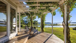 A covered outdoor deck with a view of a lake and grassy area.